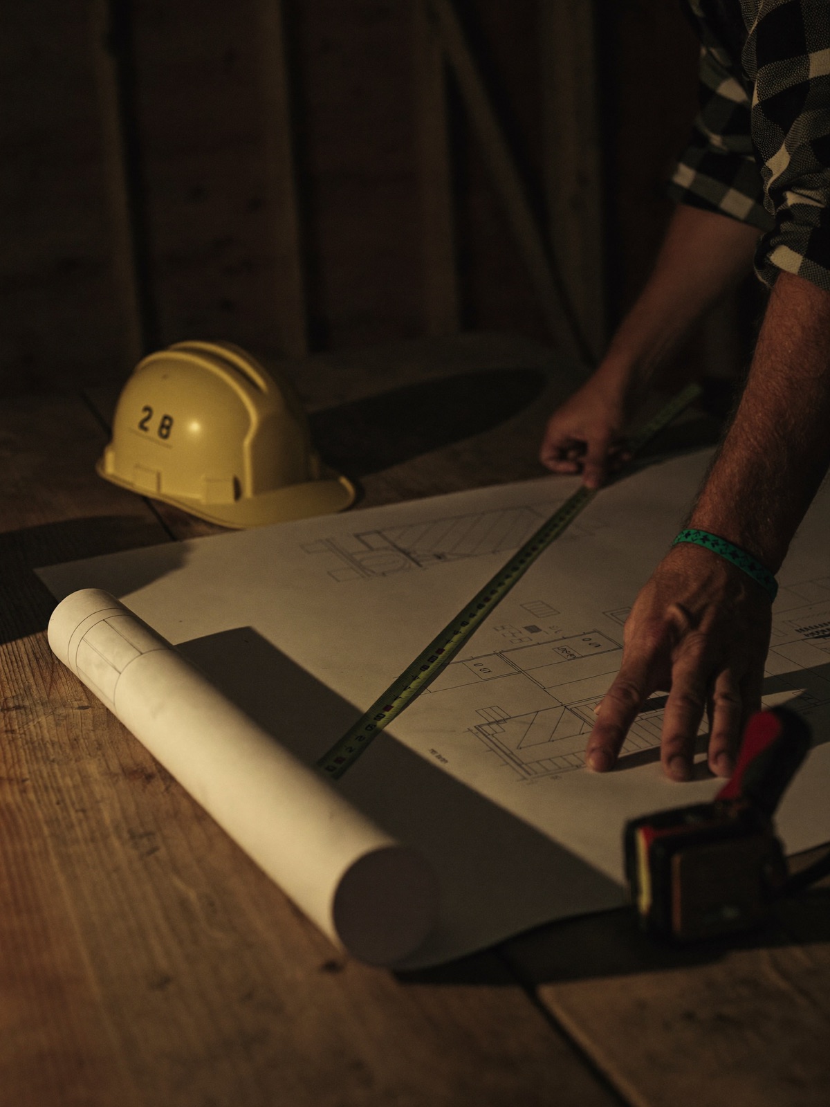 Mains de travailleurs penchés sur des plans de construction, casque de sécurité posé sur la table de chantier
