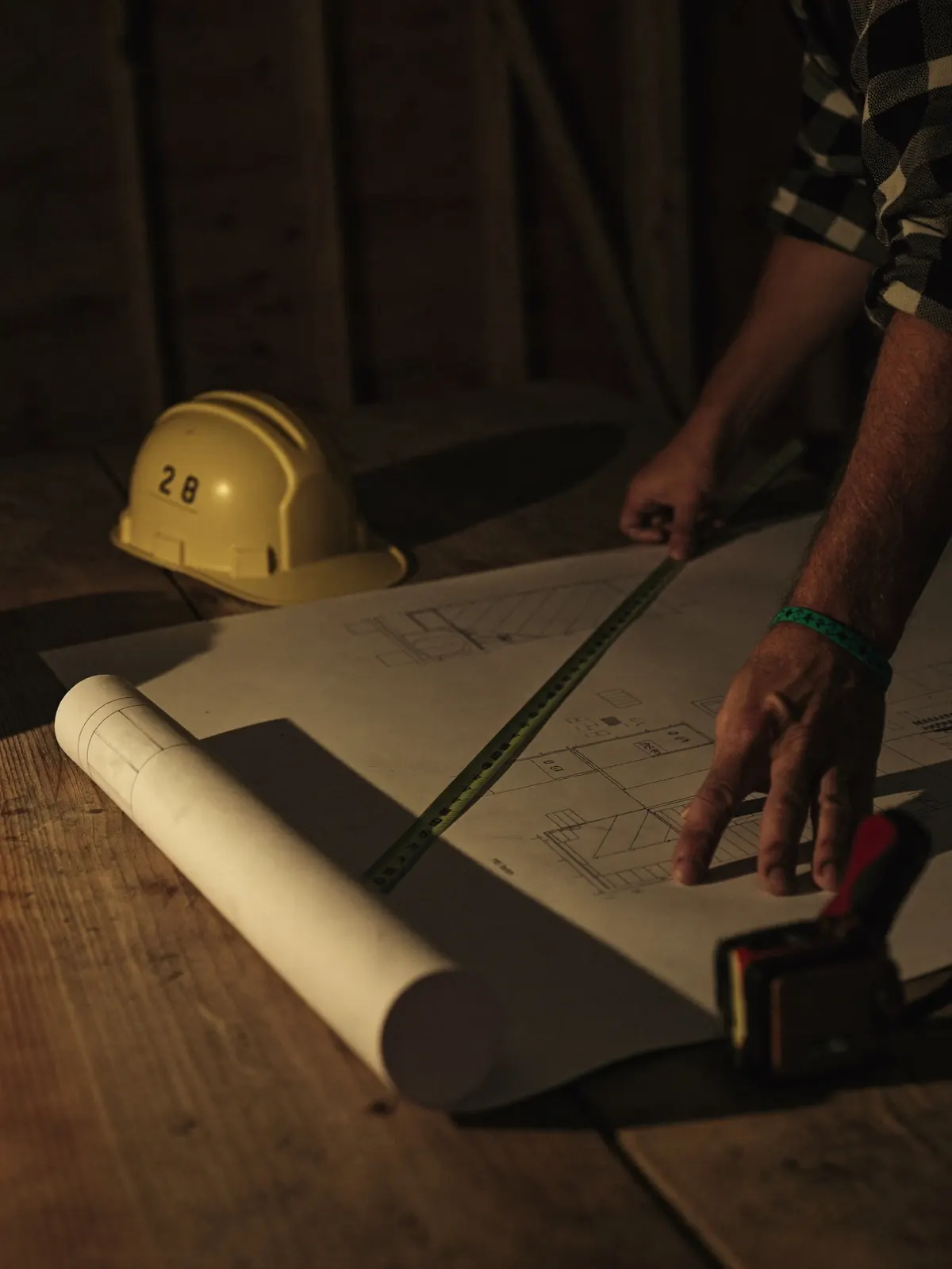 Mains de travailleurs penchés sur des plans de construction, casque de sécurité posé sur la table de chantier