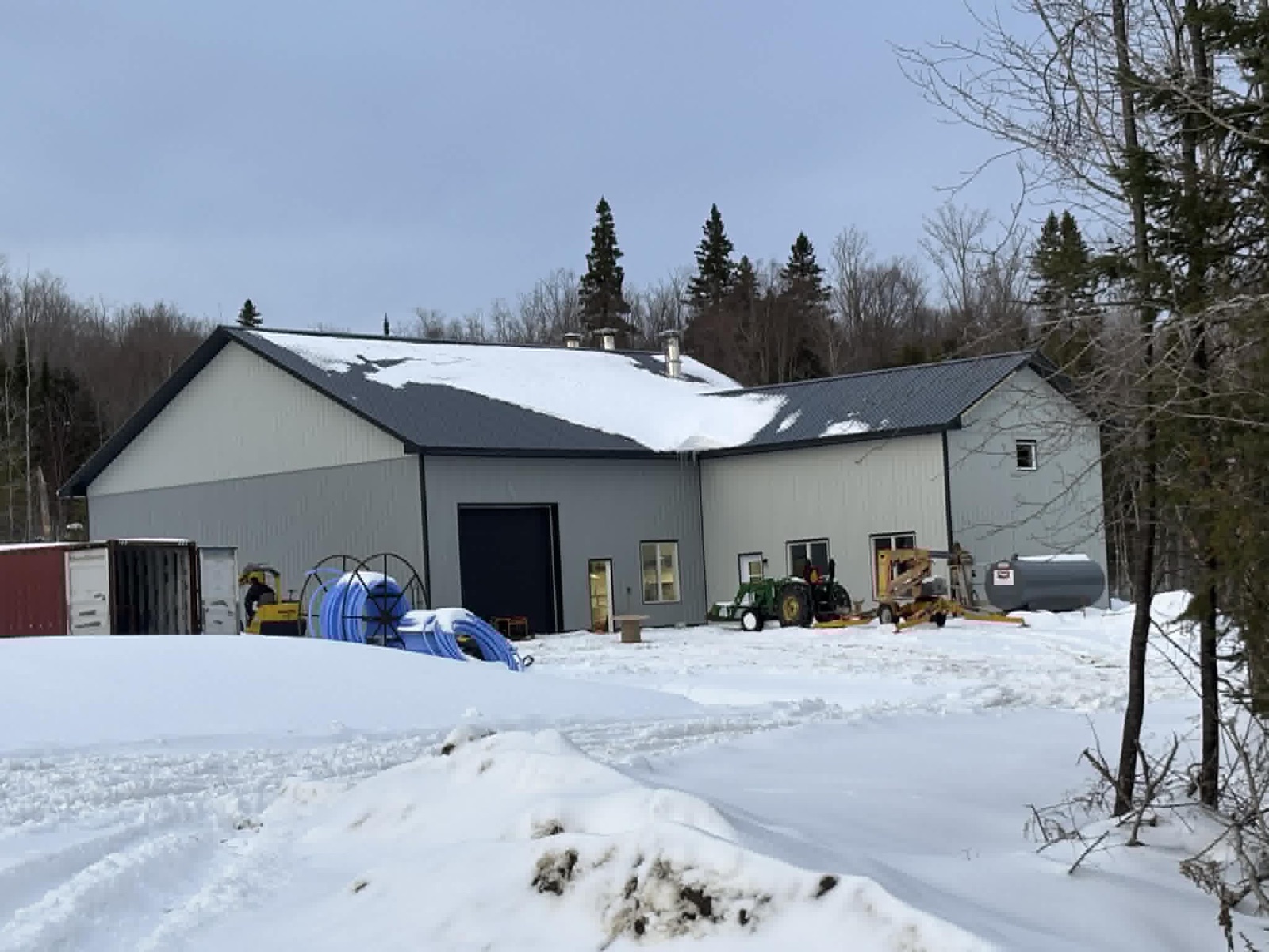 Cabane à sucre en acier gris construite par Construction Provençal pour un producteur acéricole, tracteur et tubulure devant le bâtiment