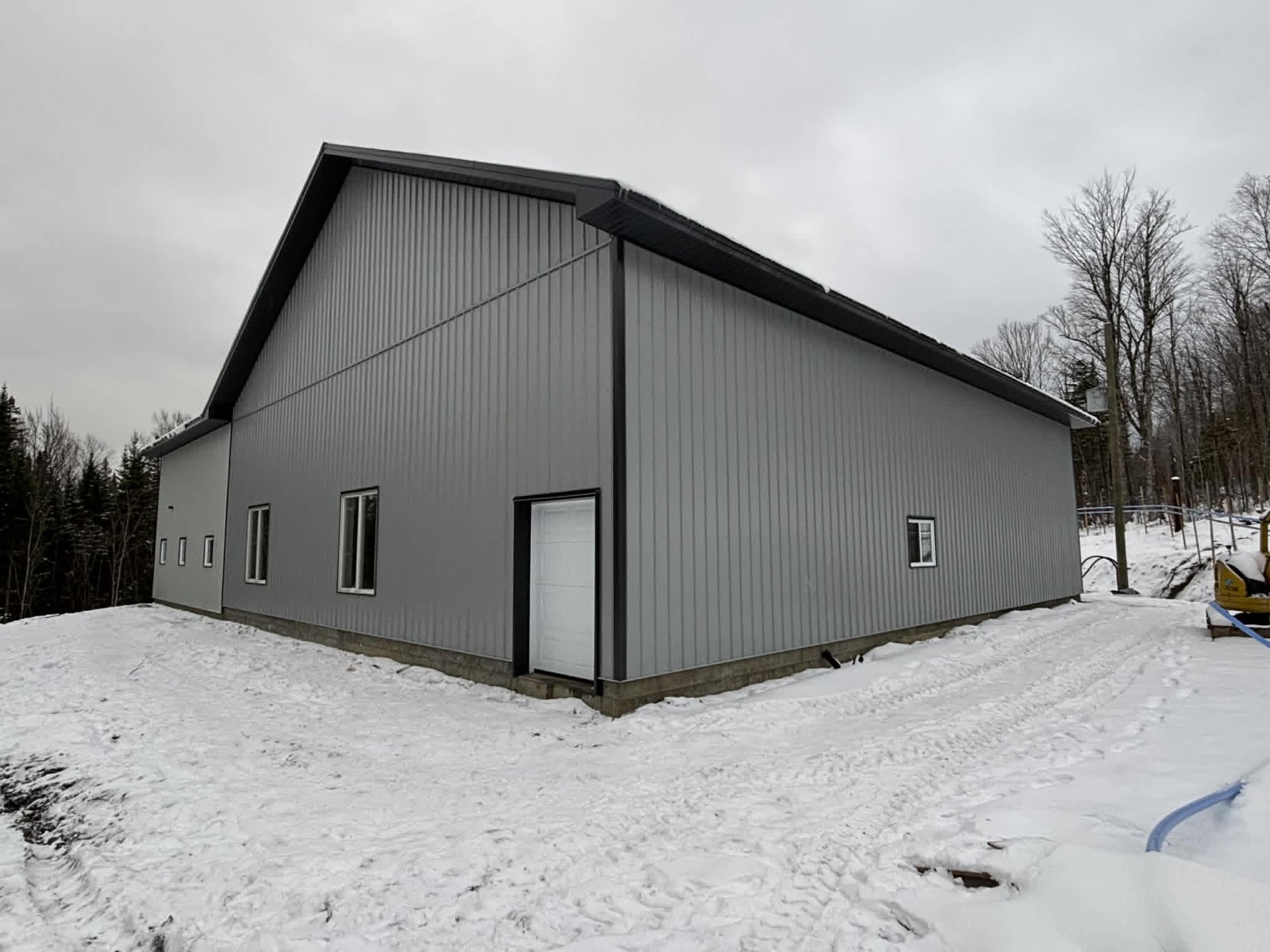 Bâtiment acéricole en acier gris et noir sous la neige, vue de côté