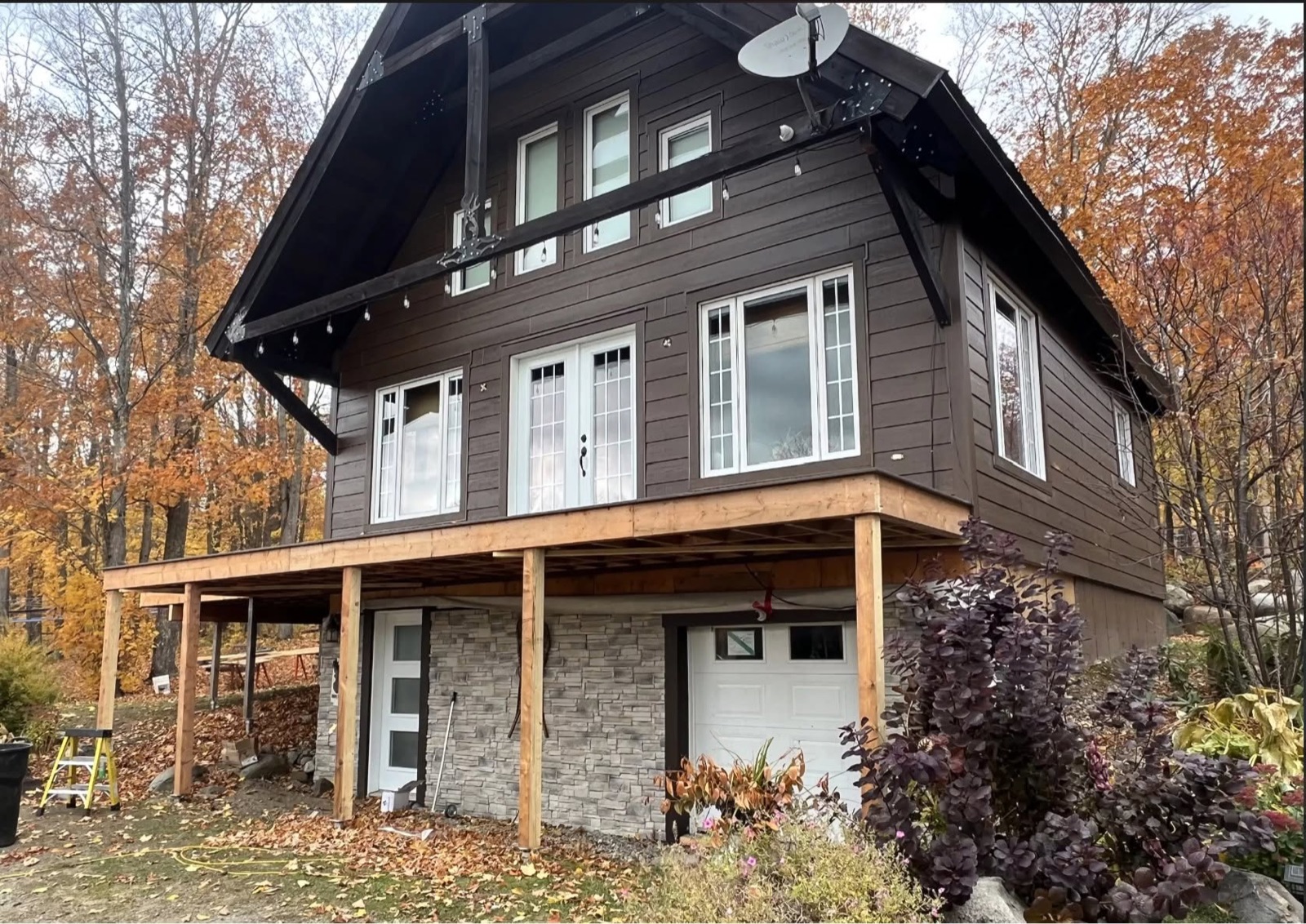 Chalet brun en bois avec soubassement en pierre et galerie sur poteaux, en automne, réalisé par Construction Provençal