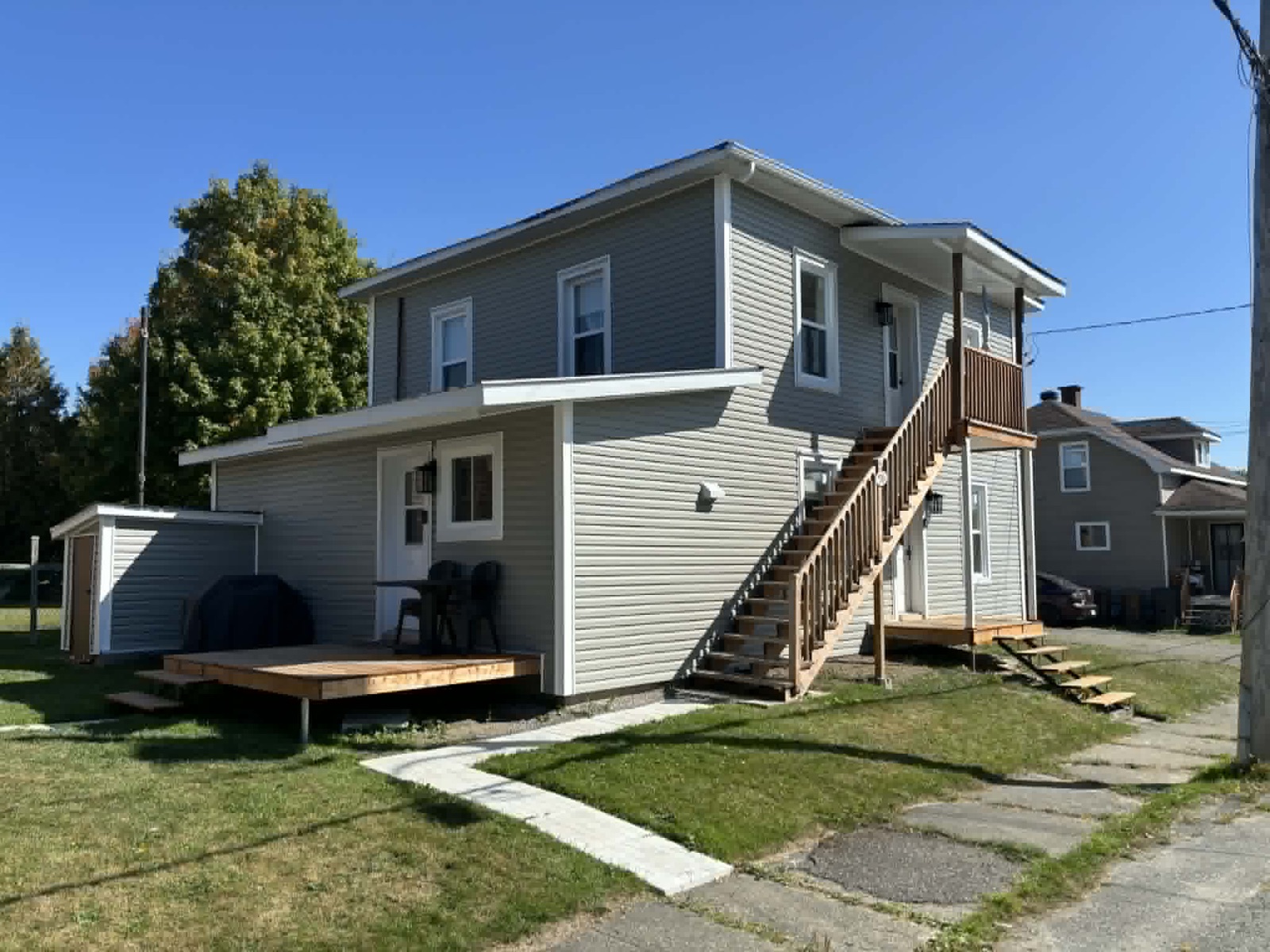 Duplex rénové : revêtement gris neuf, escalier extérieur et terrasses de bois