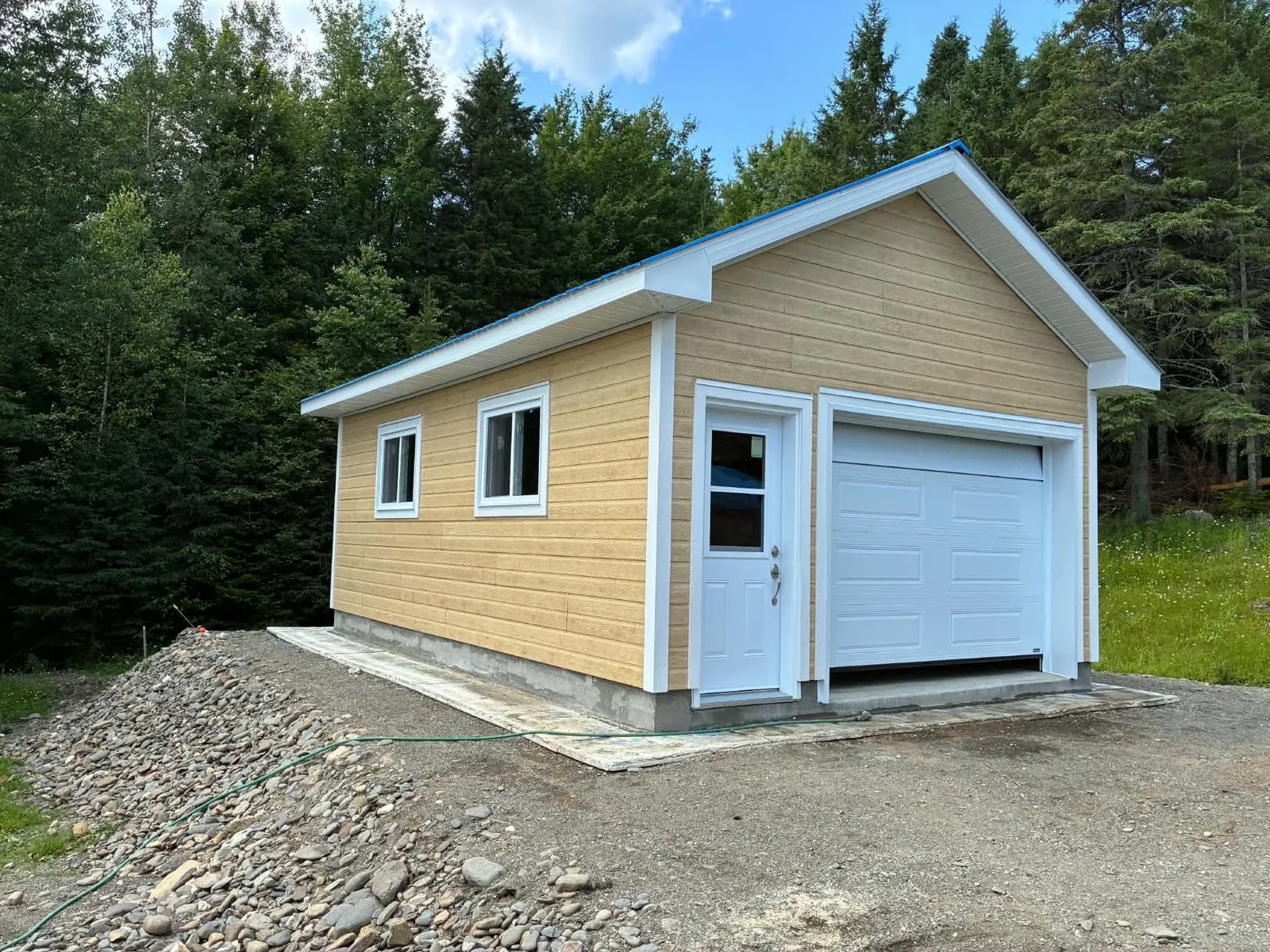 Garage détaché neuf vu de trois quarts, revêtement de bois beige, fenêtres et portes blanches, construit de A à Z par Construction Provençal